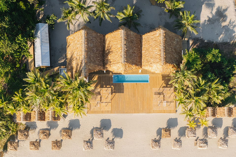 Aerial view of Duna Beach Club with thatched-roofs, pool, and palm trees at Indura Beach & Golf Resort