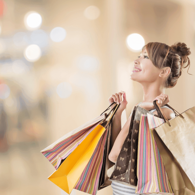 Cheerful woman holding several shopping bags and looking up at a bright display at Warwick Hotels and Resorts
