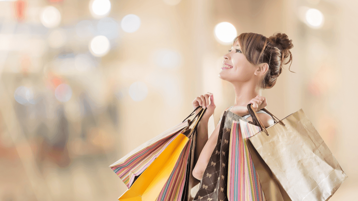 Cheerful woman holding several shopping bags and looking up at a bright display at Warwick Hotels and Resorts