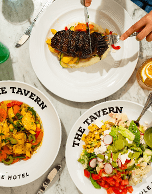 A table with three plates of food and a hand holding utensils