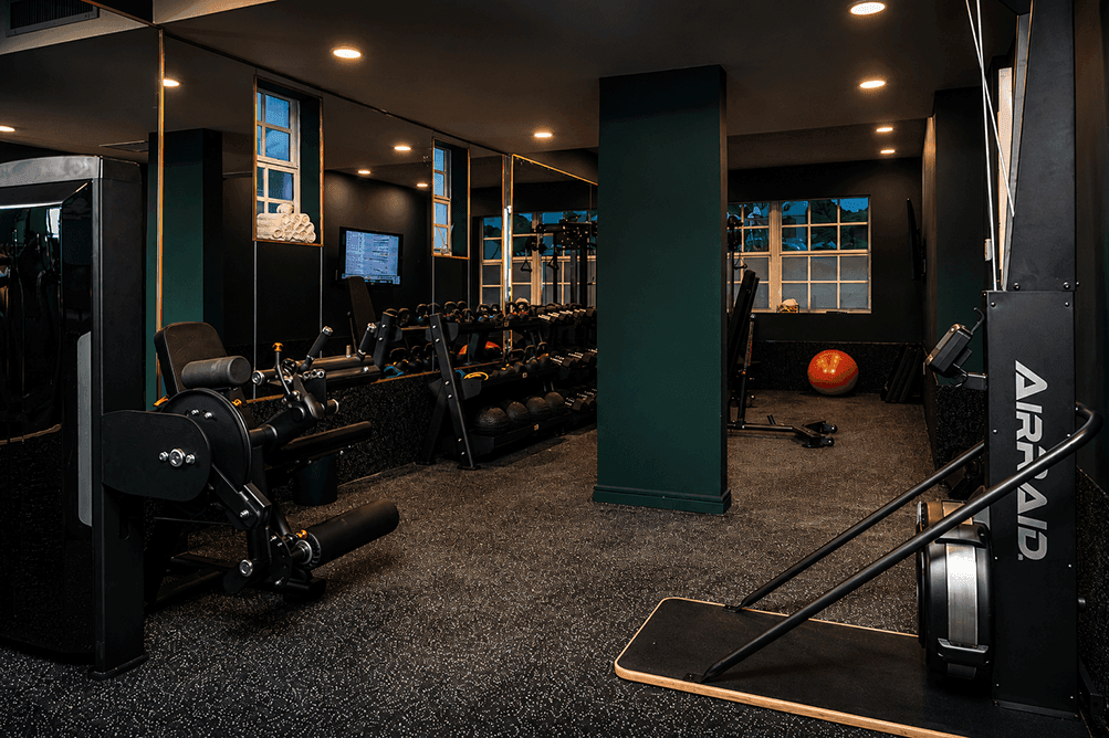 A gym with various exercise equipment and a TV screen on the wall.