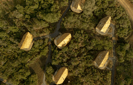 Vista aérea de cabañas con techos de paja y senderos sinuosos entre el frondoso bosque verde de Hotel Casa Selvaggio