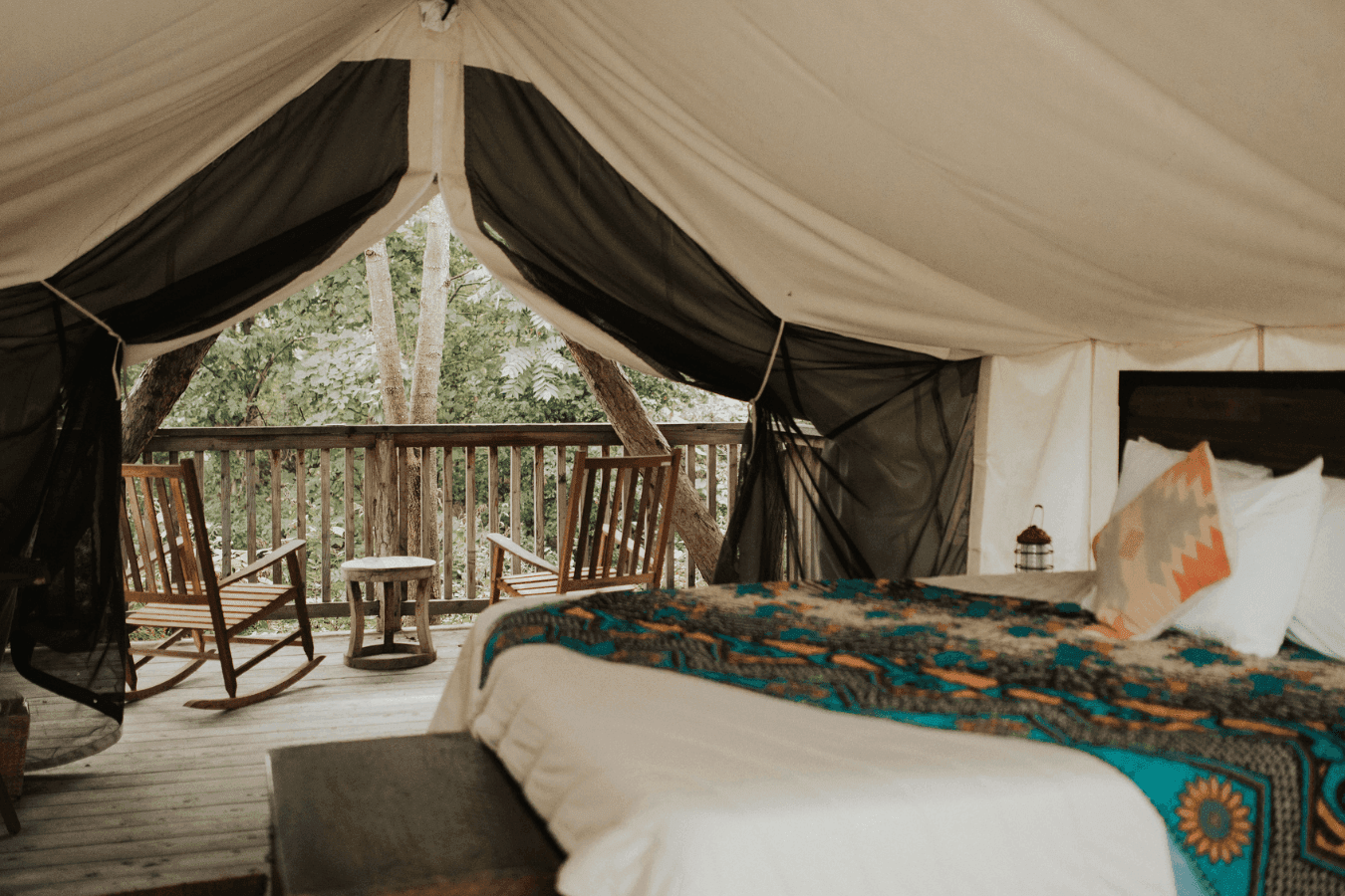 Glamping tent interior with rocking chairs by a wooden deck railing beside patterned bedding at La Tourelle Inn and Spa