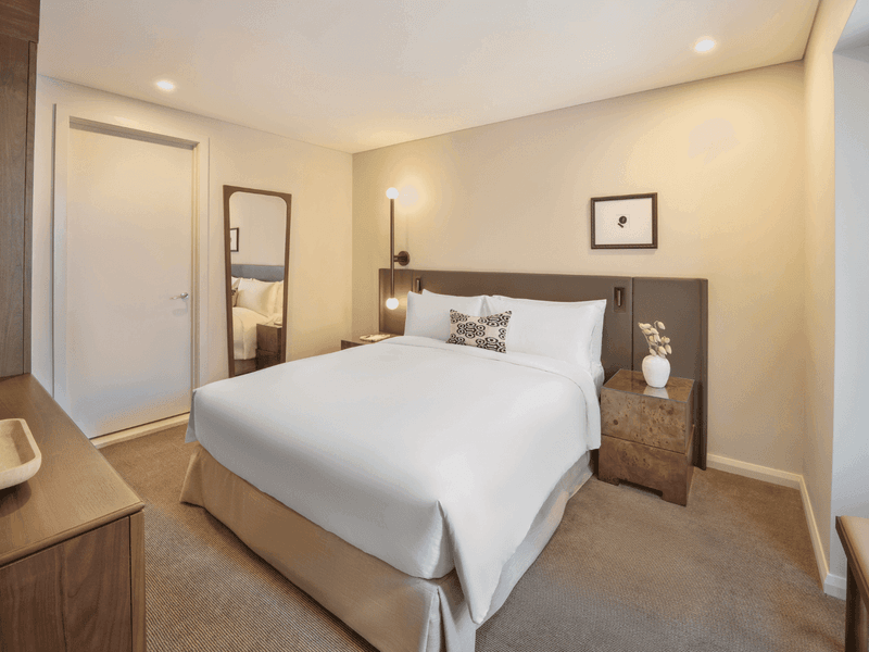 Contemporary hotel bedroom with white bedding, wooden nightstands and framed artwork above headboard