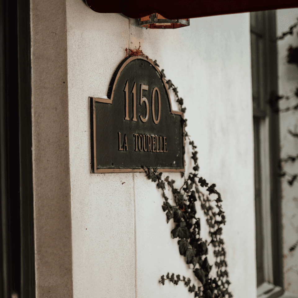 La Tourelle 1150 address plaque mounted on a white wall beside trailing ivy vines at La Tourelle Inn and Spa entrance