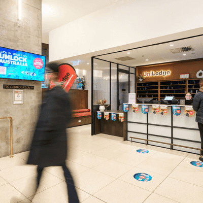 Person walking past a UniLodge reception with two people standing at the counter.