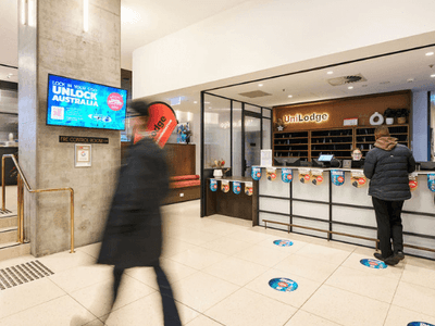 Person walking past a UniLodge reception with two people standing at the counter.