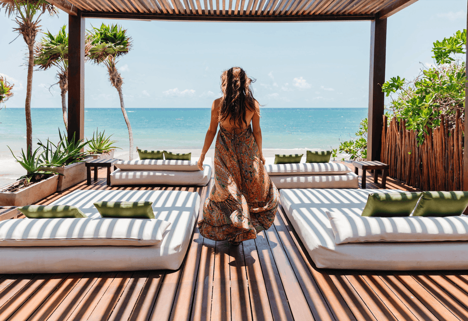 Woman in a long dress walks across a shaded deck at La Zebra Hotel toward the ocean view