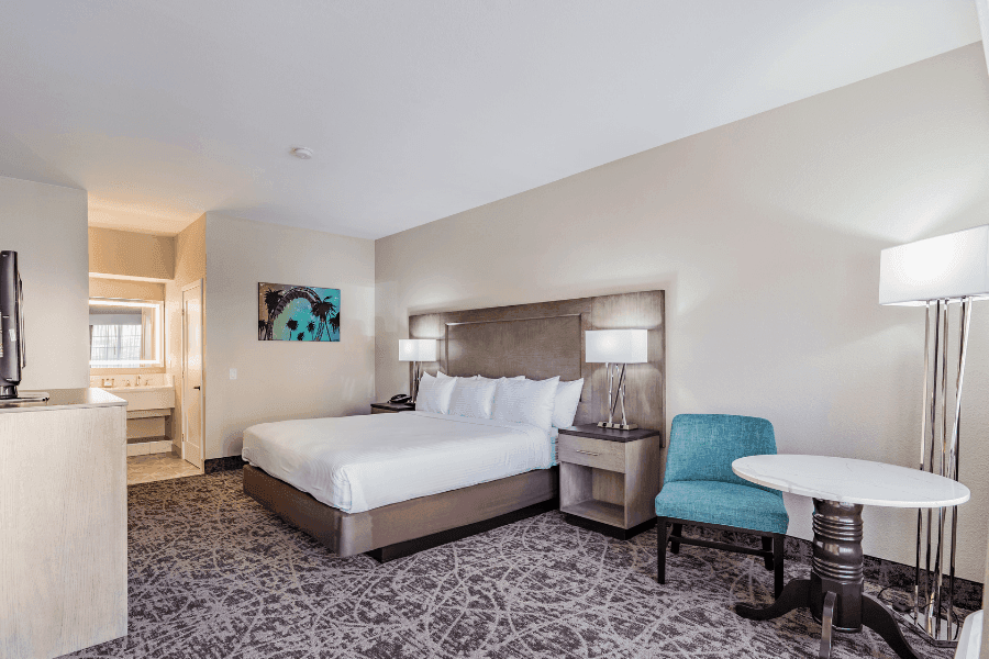 A hotel room with a bed, chair, table, and lamp