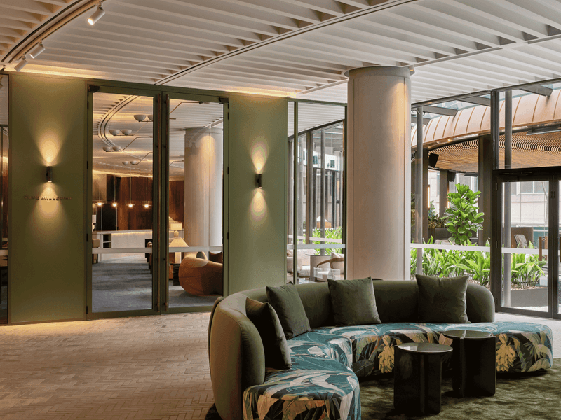 Modern lounge area with a curved couch, glass walls, and lush indoor plants, showcasing a contemporary design.