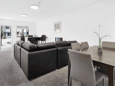 Modern open-plan living area with dark sofa, dining table, and bright natural light at Springfield Central
