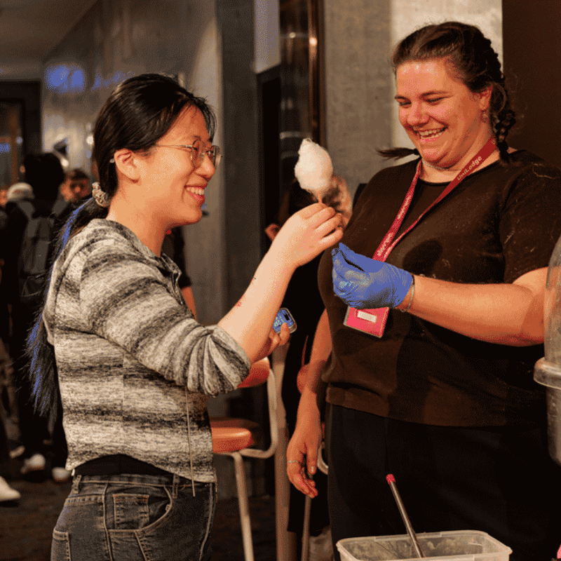 Two smiling women enjoying cotton candy at a UniLodge social event in a modern lobby setting.