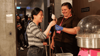 Two smiling women enjoying cotton candy at a UniLodge social event in a modern lobby setting.