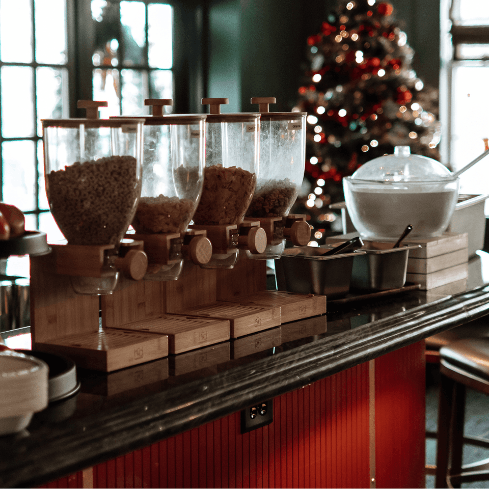 Glass cereal dispensers and metal bowls set on a bar counter beside a lit Christmas tree at La Tourelle Inn and Spa