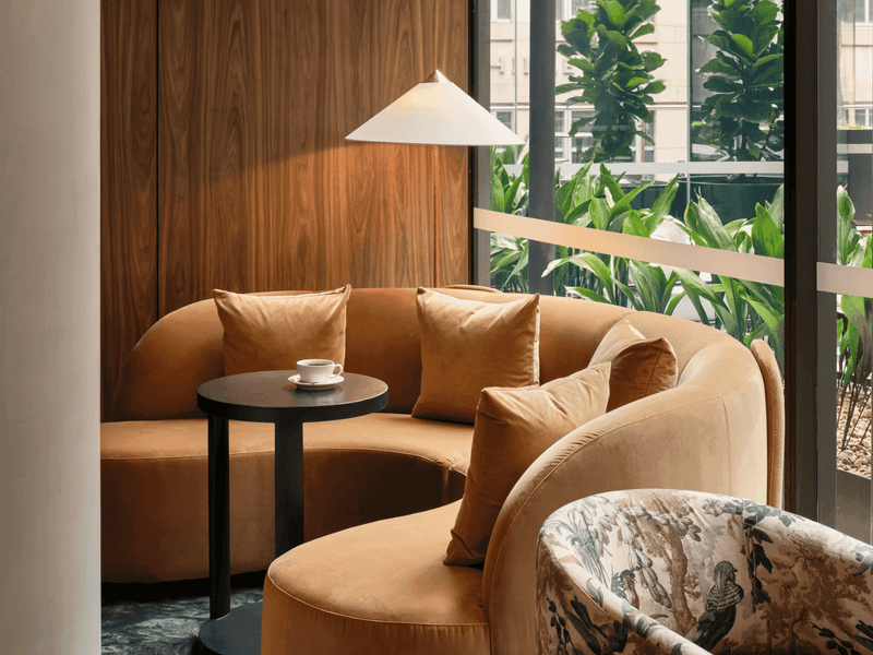 Cozy lounge with a curved couch, coffee table, and decorative chair near a large window with greenery.