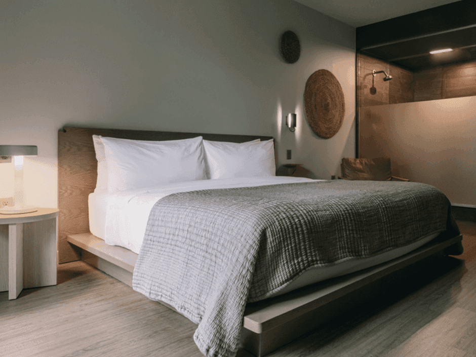 A large bed with white bedding and a gray blanket, flanked by nightstands and lamps, in a minimalist room.