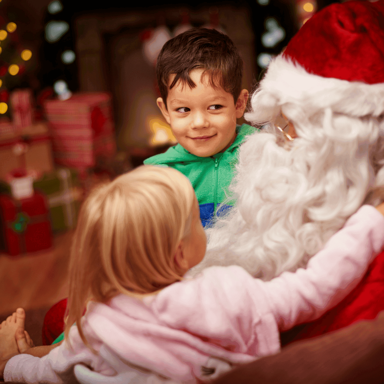 Santa Claus embraces two children, a boy and a girl, in a festive holiday setting.