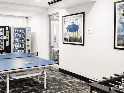 Modern recreation room with ping pong table, foosball, vending machines, and contemporary artwork on white walls.