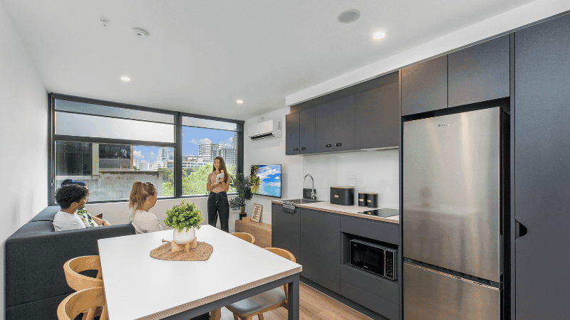 Modern living space with dining area, kitchen, and large windows showing city view.