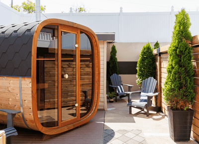 Modern barrel sauna with glass door situated on a private patio beside potted evergreen cedar trees at Rodd Moncton