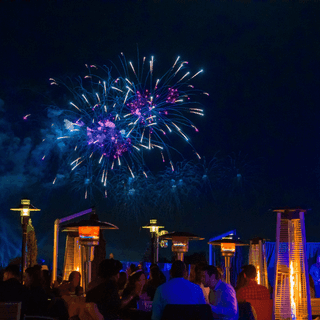 Colorful fireworks burst over illuminated structures as crowds watch the nighttime display at a theme park.