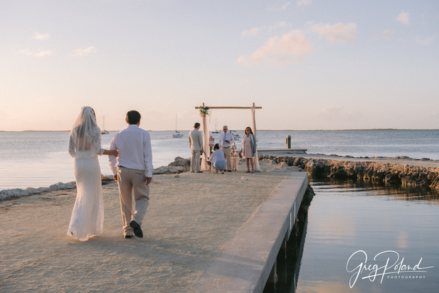 Bride walking down jetty towards groom surround by the family at Bayside Inn Key Largo