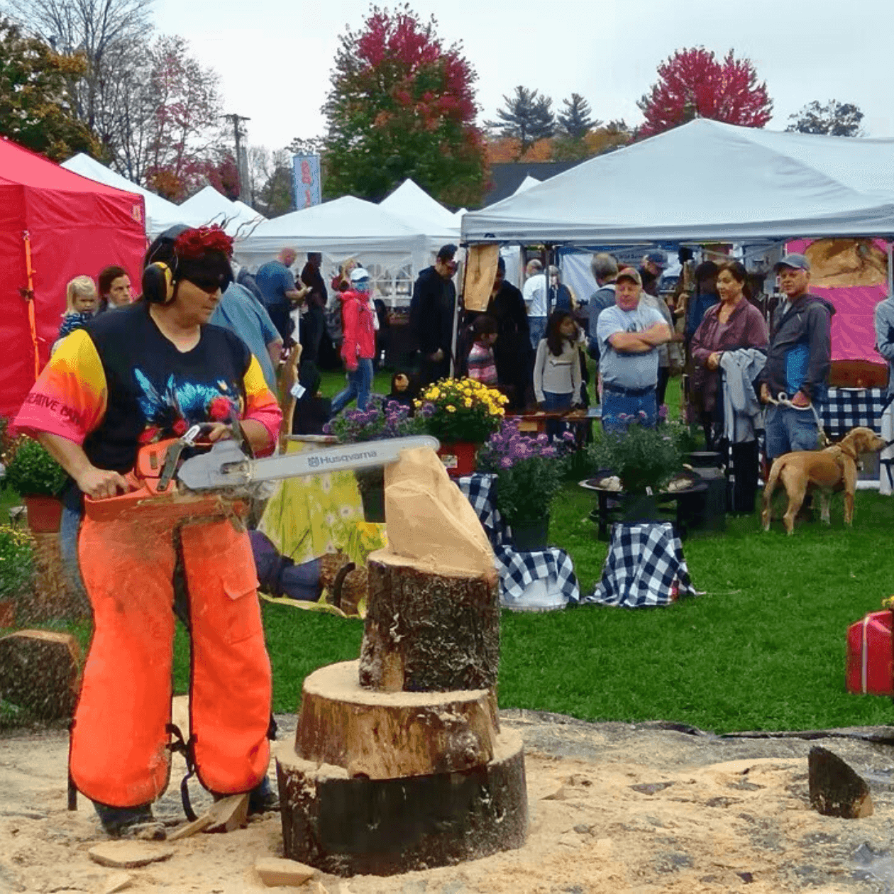 Wood carver sculpting a log with a chainsaw at an outdoor fall festival near tents by Grand Summit Hotel at Attitash
