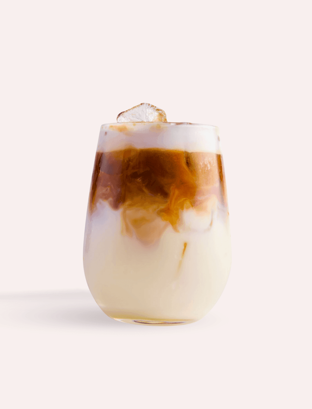 Glass of iced latte with layers of dark coffee and creamy milk, topped with ice served at The Londoner Hotel