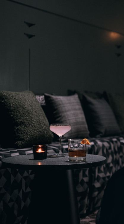 A pink cocktail and a wiskey glass set next to a mondern dark blue chair