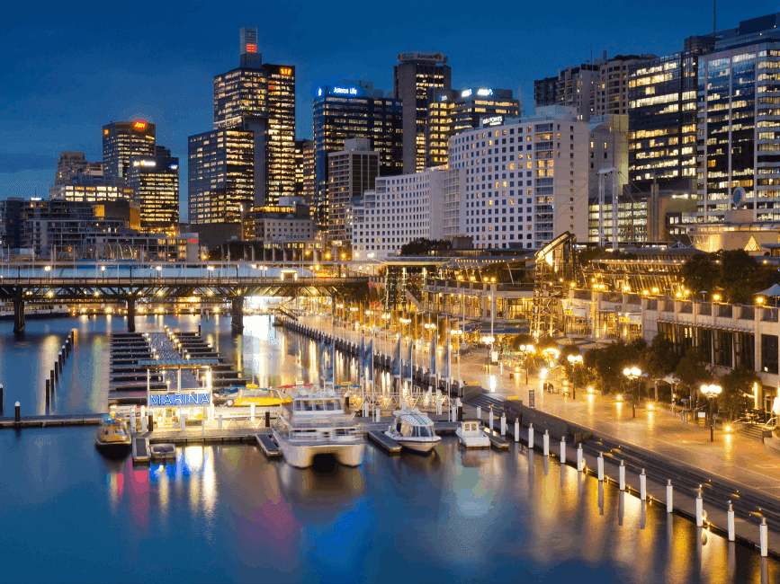 Illuminated Darling Harbour with a marina, bridge, and city skyline at night.