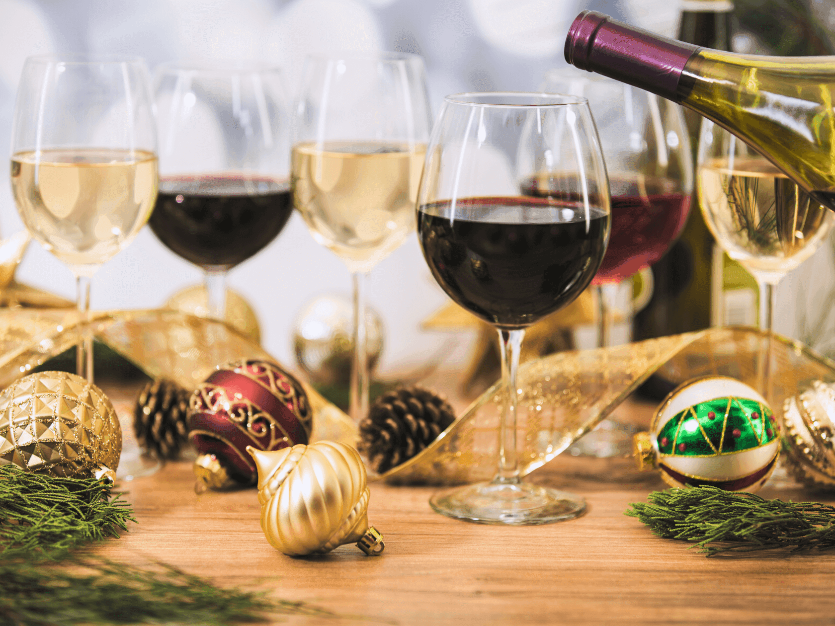 A table set for a holiday party with two glasses of red wine and three glasses of white wine.