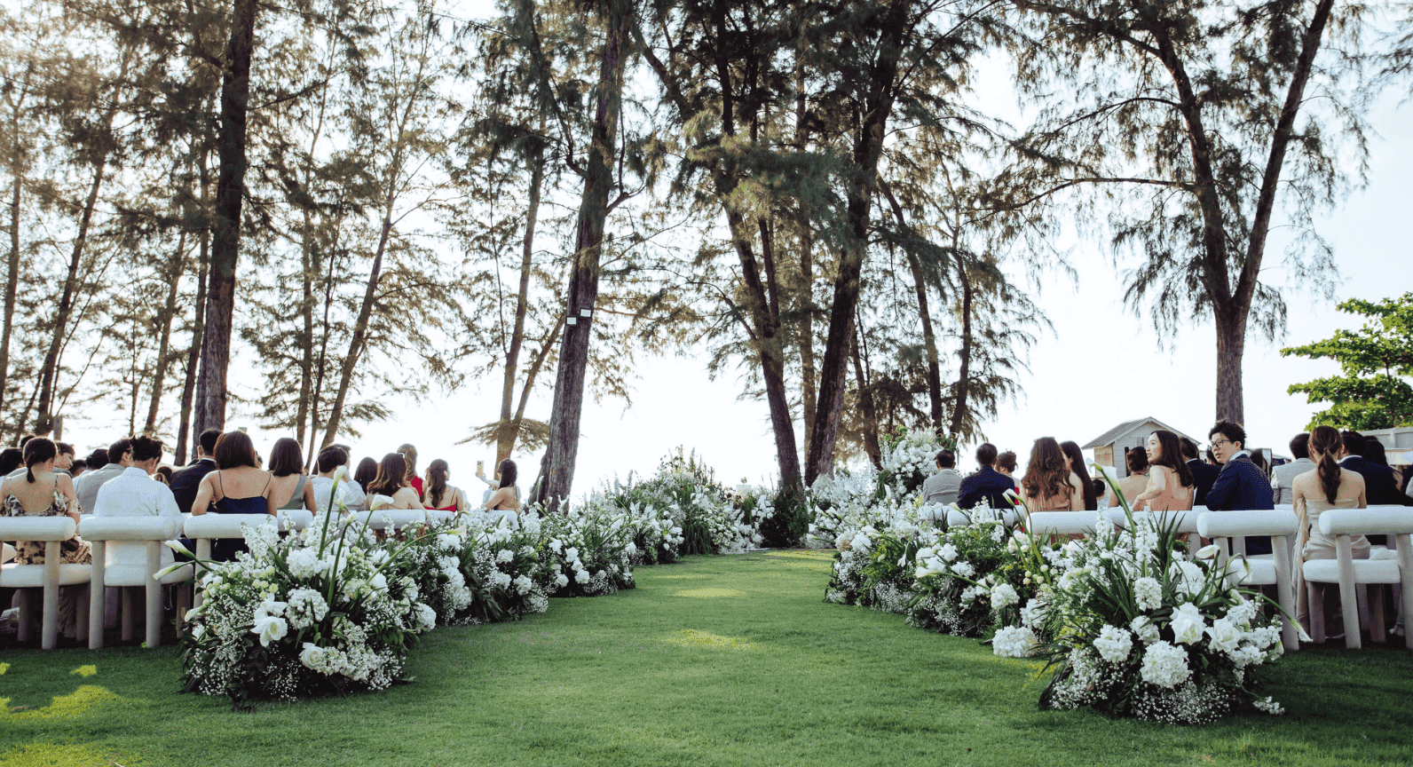 An outdoor wedding ceremony with floral arrangements along the aisle and guests seated at Amora Beach Resort Phuket