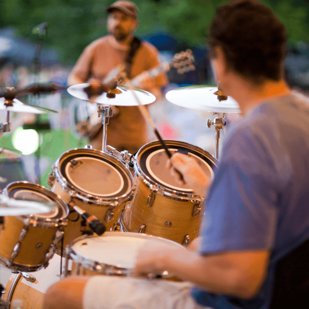 Two musicians performing outdoors, one playing drums and cymbals, the other playing a guitar.