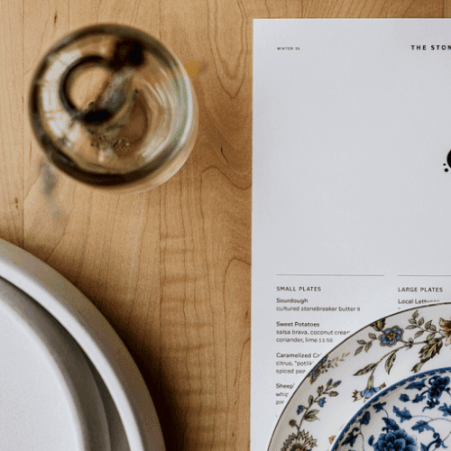 Floral-patterned plates and a menu from The Stonebreaker restaurant on a wood table.