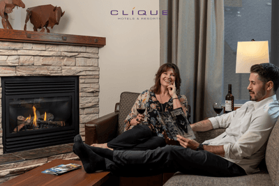 Relaxed couple enjoys wine by the fireplace in their cozy suite at Falcon Crest Lodge, looking through travel brochures