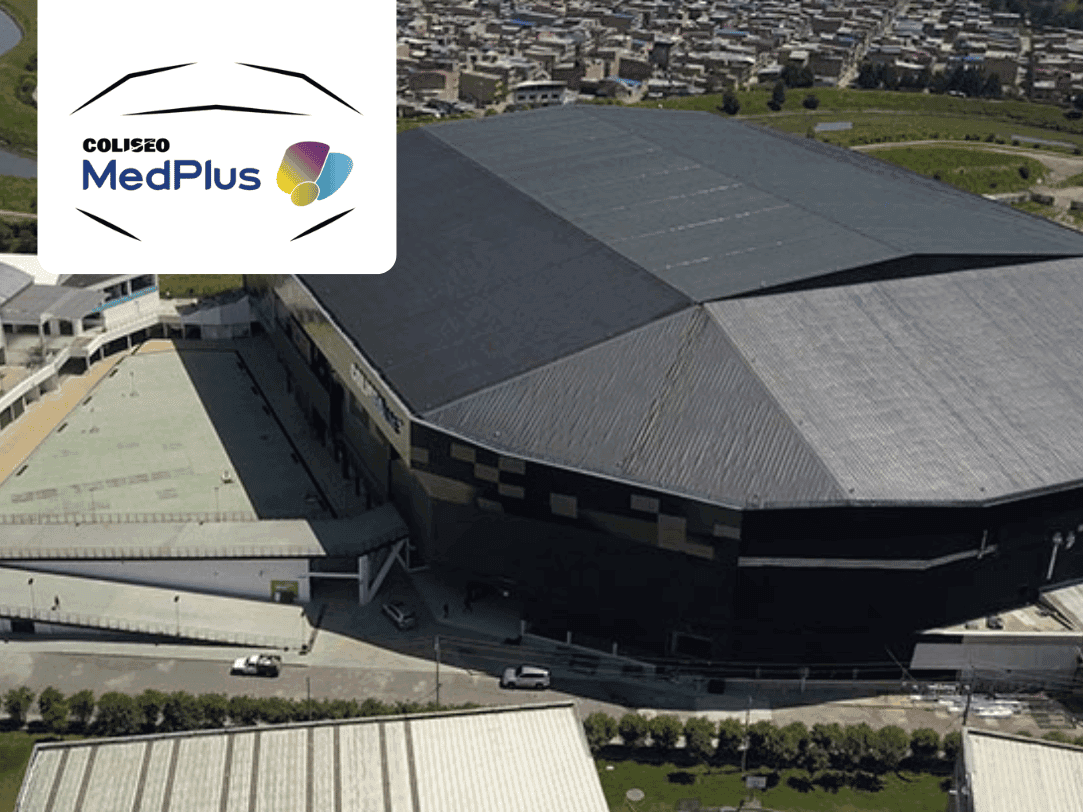Gran estadio o arena moderna de usos múltiples con un distintivo techo oscuro y la infraestructura circundante, incluyendo una cancha deportiva adyacente, identificado como Coliseo MedPlus