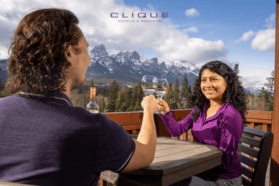 Couple clink wine glasses in a toast, with a blurred bottle in the foreground and a majestic view at Falcon Crest Lodge