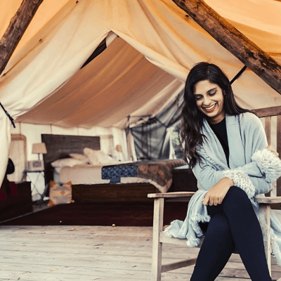 Woman sitting on a wooden chair inside a glamping tent with a bed in the background at La Tourelle Hotel and Spa