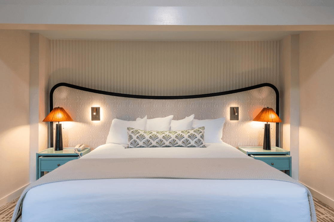 A neatly made bed with white bedding and pillows, flanked by two nightstands with lamps, in a room with a distinctive headboard.