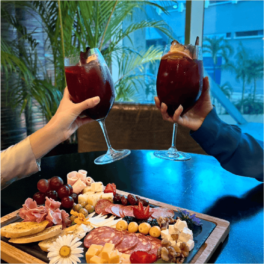 Dos huéspedes brindan con sangría roja sobre una tabla de embutidos, queso y uvas en Megapolis Hotel Panama
