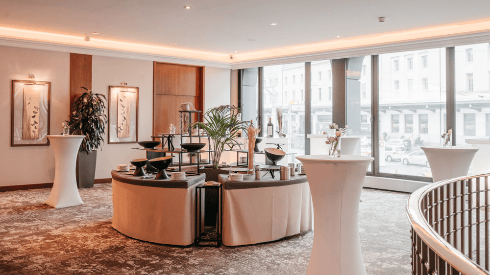 Catering tables surrounding a central plant by tall windows in Foyer Mezzanine at Warwick Geneva