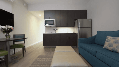 Living area with blue sofa by an ottoman and dining table beside a full modern kitchenette at Star Suites Vero Beach