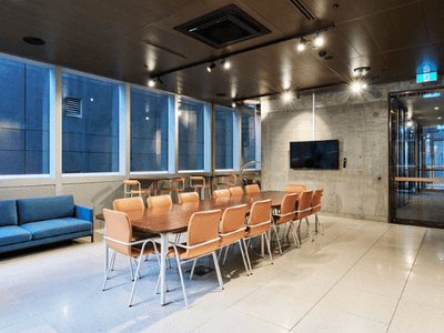 Modern meeting room with large windows, blue couch, wooden table, and chairs, and a flat-screen TV.