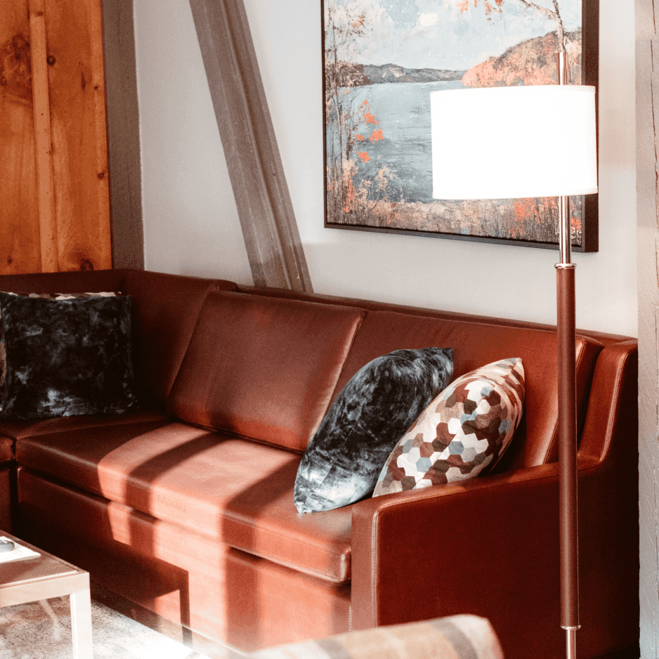 Leather sofa with patterned throw pillows beside a floor lamp under framed lake artwork at La Tourelle Inn and Spa