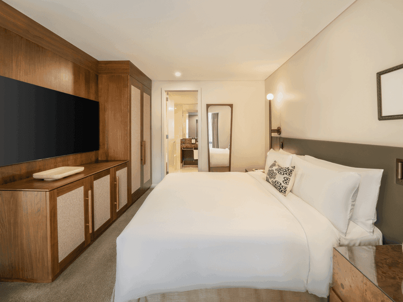 Modern hotel room with king bed, wooden headboard, wall-mounted TV and built-in desk area