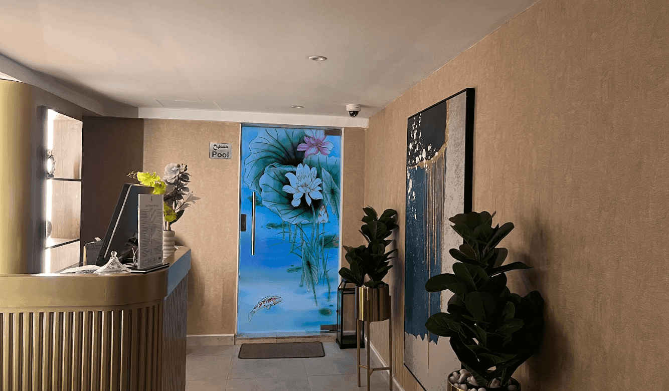 Swimming Pool Entrance at Warwick Al Jubail with a gold desk by a floral glass door & potted plants