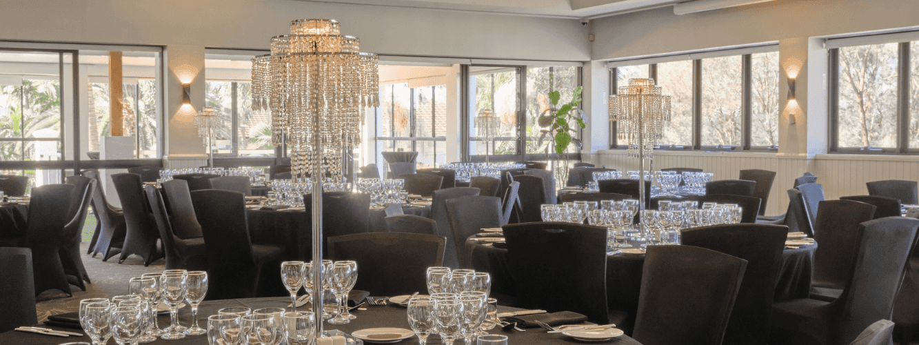A large, well-decorated banquet hall with many tables set for dining, large windows, and crystal chandeliers.