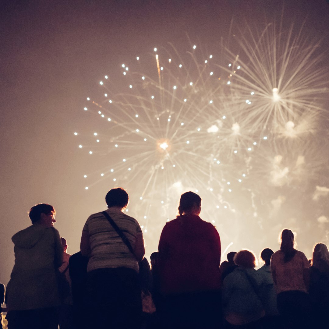 A crowd of on lookers watching the night sky light up by new year's fireworks.