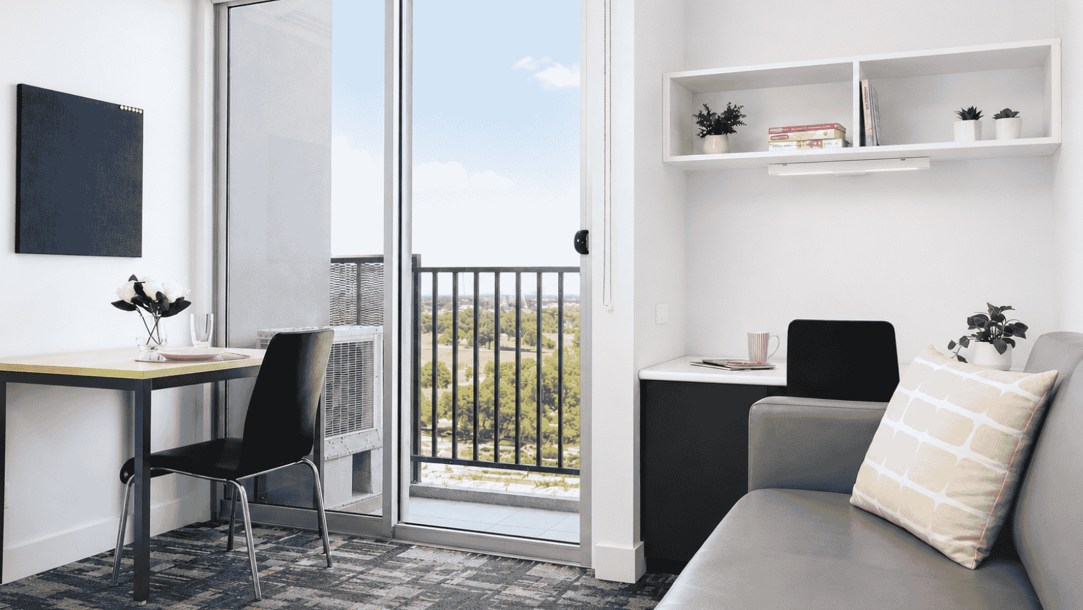 Modern student living room with desk, gray sofa, white shelving, and balcony access with city views at Student Living - Waymouth