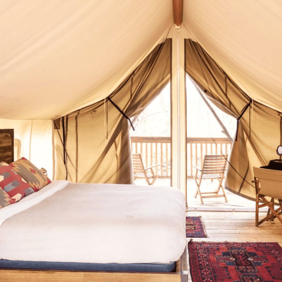 Firelight Camps tent featuring a comfortable bed beside a small desk with a balcony view at La Tourelle Hotel and Spa